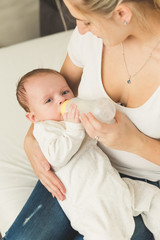 Young mother feeding her baby boy in bed from bottle