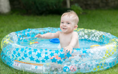 Fototapeta na wymiar Cute 9 months old baby boy having fun in inflatable swimming pool