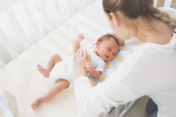 Mother sitting near the cradle and holding baby's hand