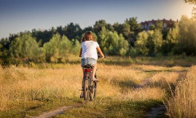 Beautiful girl in t-shirt cycling in meadow at sunset