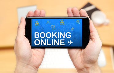 Watching two hand holding mobile phone with Booking online word on screen and blur desk office background,Digital reservation concept