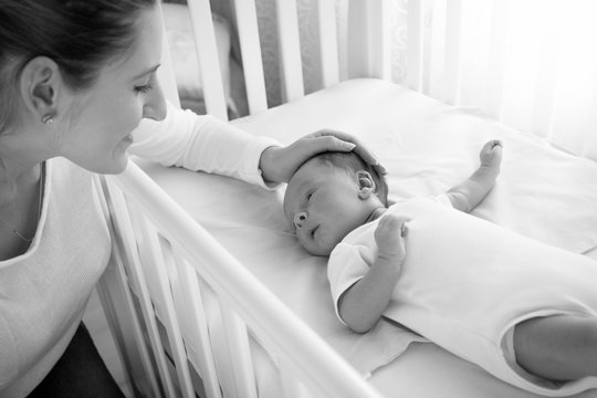 Black And White Portrait Of Happy Smiling Mother Caressing Her Baby Lying In Cot