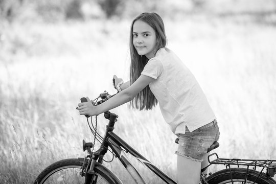 Monochrome image of beautiful teenage girl riding bicycle at meadow