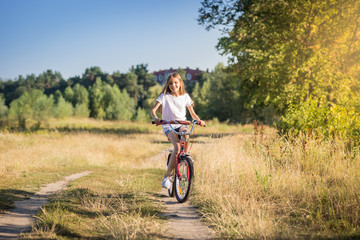 Happy young girl riding bike in meadow at sunny day