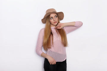 Cute and stylish beautiful young blonde woman in trendy clothing practicing model poses and looking away with smile while standing against white wall background