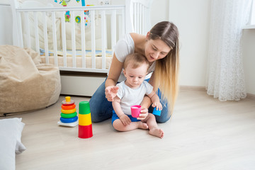 Young mother playing and teaching her baby boy on floor at living room