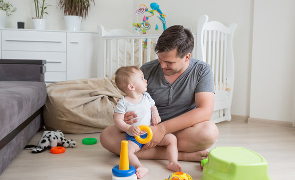Cheerful father playing with his baby boy on floor at living room