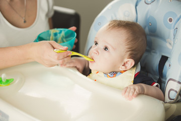 Mother giving porridge to her baby boy from plastic spoon