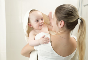 Smiling mother covering baby in towel after having bath