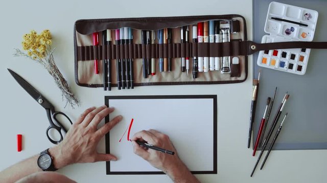 Top view on blank sheet of paper next to calligraph set of pens and markers and artist accurately writes word Adventure on it with red thick watercolor marker.