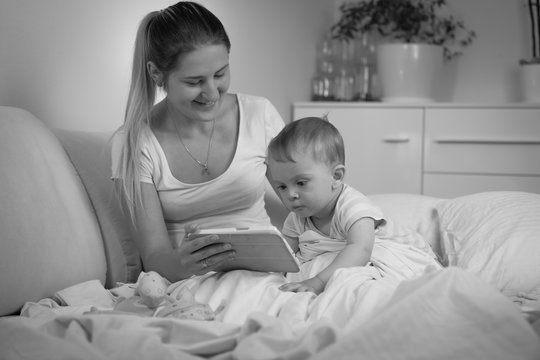 Black and white image of baby with mother using tablet computer in bed at night