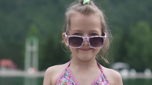 Little beautiful girl in a swimsuit and sunglasses smiling and posing at the camera. Slow motion