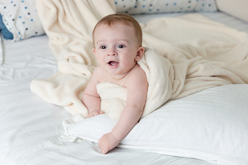 Cheerful baby boy lying on big pillow under white blanket