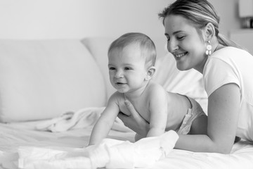Black and white portrait of happy smiling baby siting with his mother on bed at bedroom