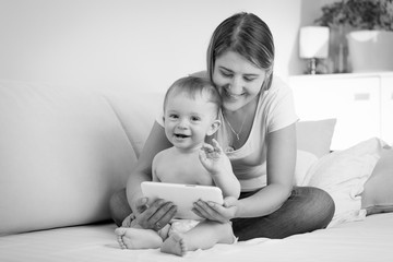 Black and white image of happy cheerful baby boy playing on tablet PC with mother