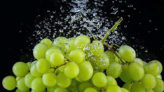 Two clusters of juicy green grape dropping into the water in slow motion. Shooting with high-speed camera.
