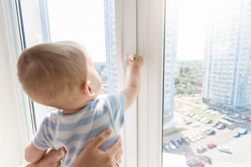 Mother holding baby boy while he is looking outside through window