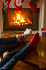 Family in knitted woolen socks warming at burning fireplace at house