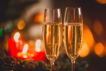 Closeup image of two glasses of Champagne in front of burning candles and lights.