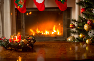 Christmas background with burning candles on wooden table in front of fireplace and Christmas tree