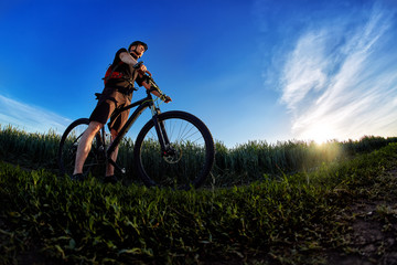 Wide angle of the cyclist standing on the trail on the field against beautiful landscape.