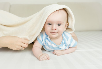 Cute smiling 6 month baby boy lying under the blanket on bed