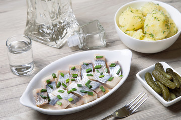 Pieces of herring with onions, gherkins, boiled potatoes and vodka. Selective focus