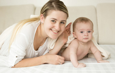 Happy smiling mother and baby covering with blanket on bed