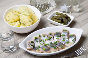 Pieces of herring with onions, gherkins, boiled potatoes and vodka. Selective focus