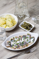 Pieces of herring with onions, gherkins, boiled potatoes and vodka. Selective focus