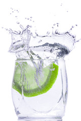 Fresh green lemon drops into a glass with water