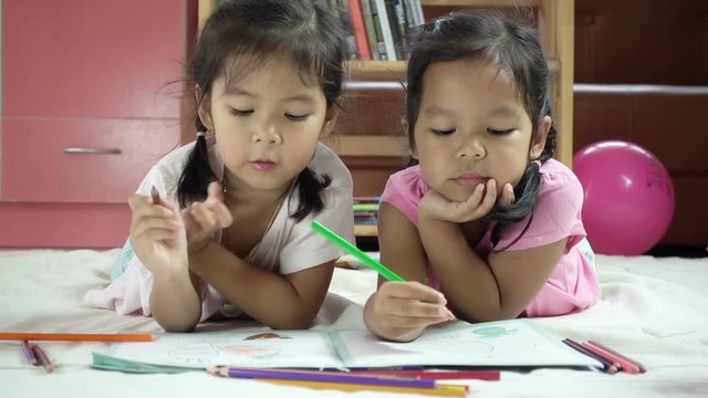 Two cute asian little girls having fun to  paint with crayon together 