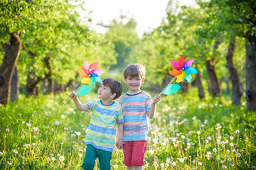 Two happy children playing in garden with windmill - obrazy, fototapety, plakaty