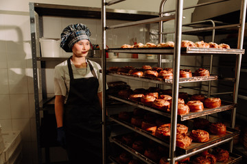 Fototapeta na wymiar Baker stands near shelves with fresh rolls