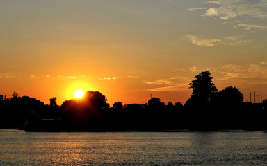 Sunset with city and threes in front of river.