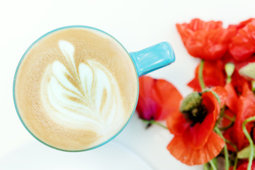 Poppy flowers and blue cup of cappuccino on white table