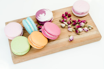 French delicious colorful macarons cookies and small roses on wood desk. White background.
