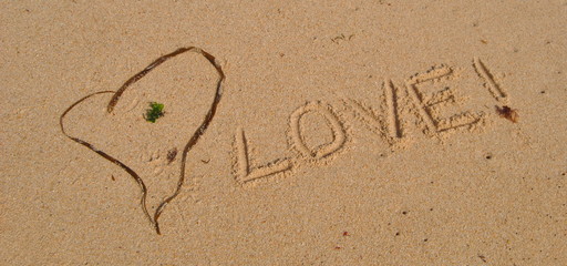 Love on sand, mensagem em inglês escrita na areia da praia com uma alga em forma de coração