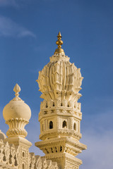 Mysore, India - October 26, 2013: Cream yellow stone corner minaret of upper structure Tipu Sultan mausoleum. Golden Kalasam on top, deep blue sky.