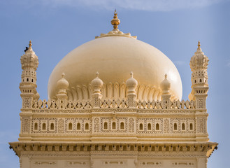 Mysore, India - October 26, 2013: Upper structure and dome of cream yellow Tipu Sultan mausoleum under blue sky. Golden Kalasam on top. One black bird.