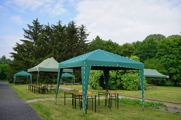Green garden tent, garden pavilion. Rest area with  chair and picnic tables and green tent installed on green lawn in a park

