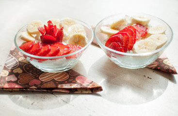 Two bowls of curd with strawberry and banana.