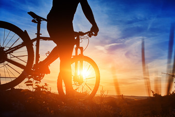 Close-up of the silhouette of young man cyclist on sunset sky with clouds.