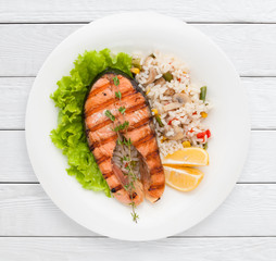 Grilled salmon steak and risotto on garnish top view. Healthy food, delicacy, lunch dish concept. White wooden planks background.