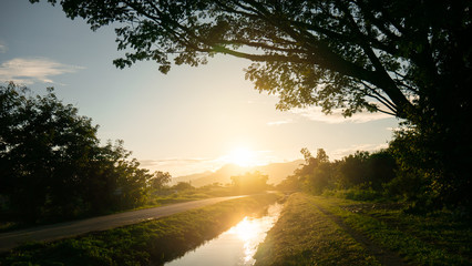 Gloden sundown and reflex water irrigation canal near small road rural.