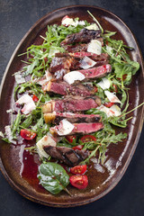 Traditional Italian Tagliata Steak with Parmesan and Salad as close-up on a plate