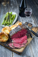 Barbecue dry aged Rib of Beef with green Asparagus and Yorkshire Pudding as close-up on an old cutting board