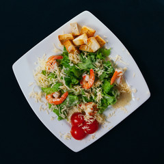 Caesar salad with shrimp on a plate. Black background
