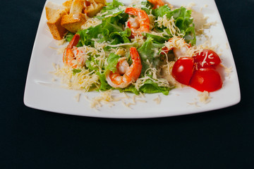 Caesar salad with shrimp on a plate. Black background