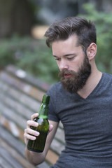 Handsome hipster guy with a bottle of beer in park
